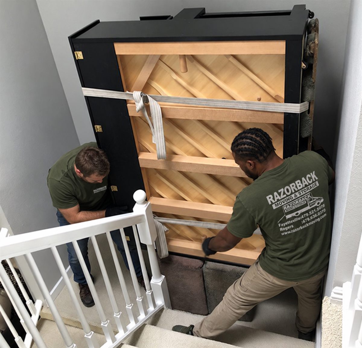 Razorback movers guiding an upright piano safely up a residential staircase